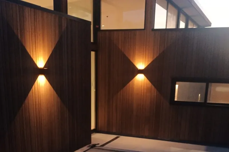 A front entrance clad in vertical cedar boards, lit by two wall lights at dusk