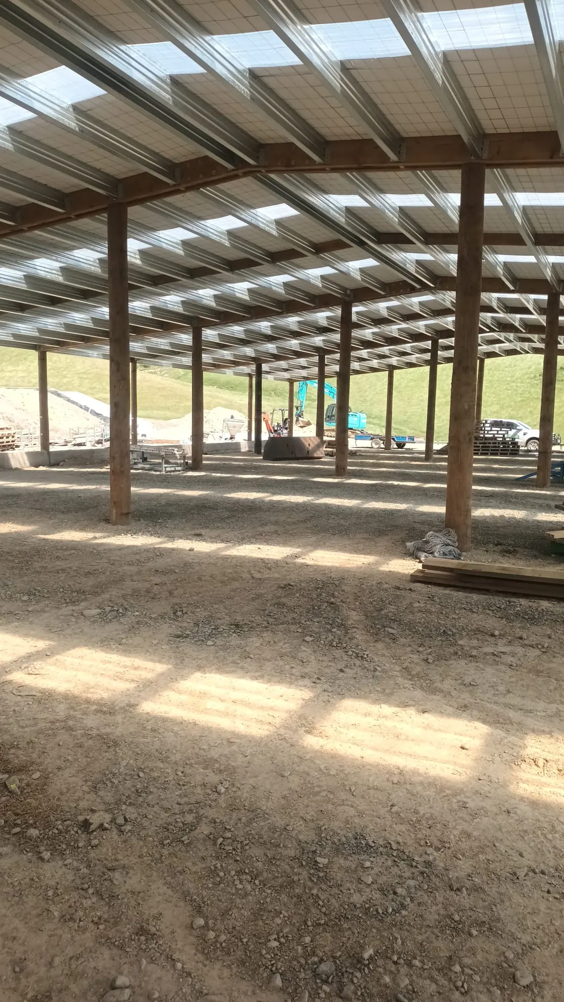 Looking along a farm shed going up, the poles, rafters and roof on and the floor still to come